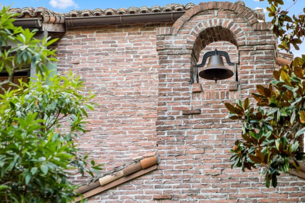 Brick exterior of luxury home featuring an architectural bell detail surrounded by lush greenery, emphasizing the elegant design of the property at 11019 Bridge House Road in Windermere, FL.
