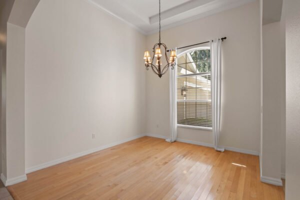 Spacious dining area with hardwood floors, elegant chandelier, and large window providing natural light, showcasing the interior of 15061 Spinnaker Cove Lane, Winter Garden, FL.