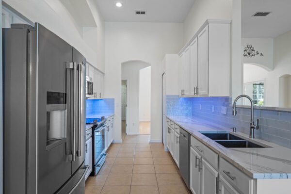 Modern kitchen with stainless steel appliances, quartz countertops, and blue under-cabinet lighting, showcasing a spacious layout ideal for family living in the remodeled pool home at 15061 Spinnaker Cove Lane, Winter Garden, FL.