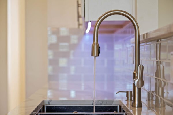 Modern kitchen faucet with running water over a sleek black sink, featuring quartz countertop and stylish backsplash, highlighting the recent remodel of the home at 15061 Spinnaker Cove Lane, Winter Garden, FL.