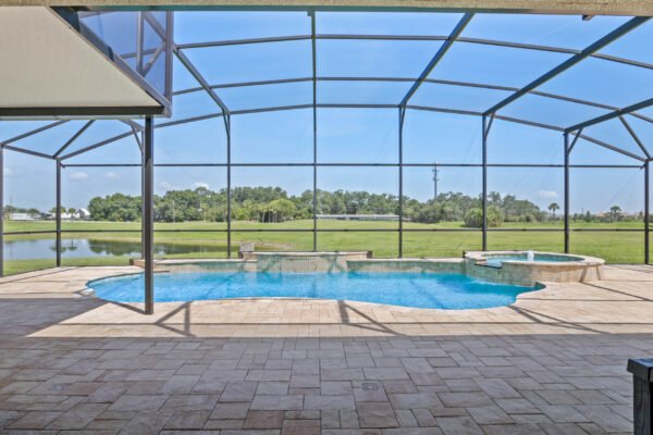 Screened-in pool area with heated pool and spa, overlooking tranquil retention pond and lush greenery, showcasing outdoor living space ideal for relaxation in Winter Garden, FL.