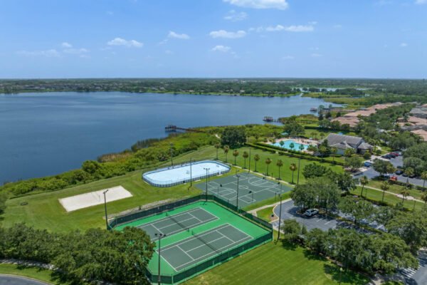 Aerial view of tennis courts, swimming pool, and scenic lake in Stoneybrook West, Winter Garden, showcasing resort-style amenities and lush greenery.