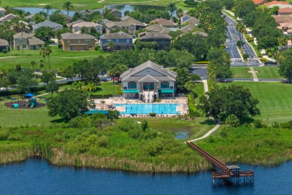Aerial view of the Stoneybrook West community clubhouse featuring a large swimming pool, playground, and scenic lakefront, surrounded by residential homes and green spaces, highlighting the resort-style amenities available in Winter Garden, FL.
