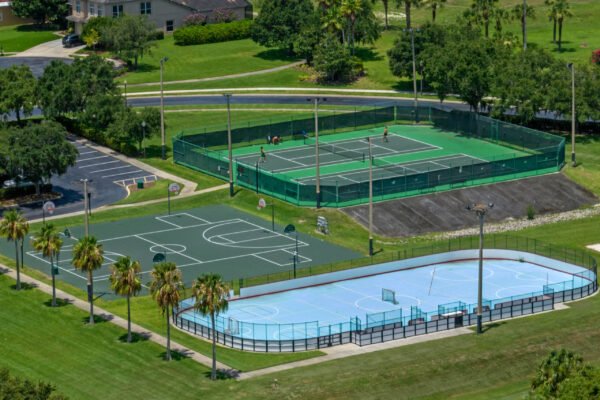 Aerial view of sports facilities in Stoneybrook West, featuring tennis courts, basketball courts, and an inline hockey rink surrounded by palm trees and green lawns.