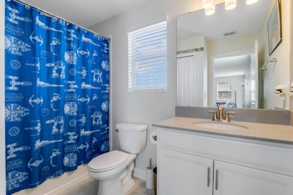 Bathroom featuring a blue Star Wars shower curtain, white vanity with gray countertop, modern fixtures, and natural light from a window, showcasing a clean and themed space ideal for a family home.