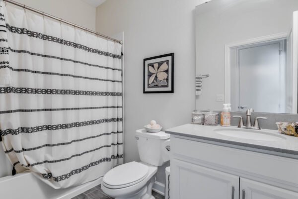 Bathroom featuring a white vanity with gray countertop, modern toilet, and a shower curtain with black and white stripes, complemented by decorative wall art and storage containers.