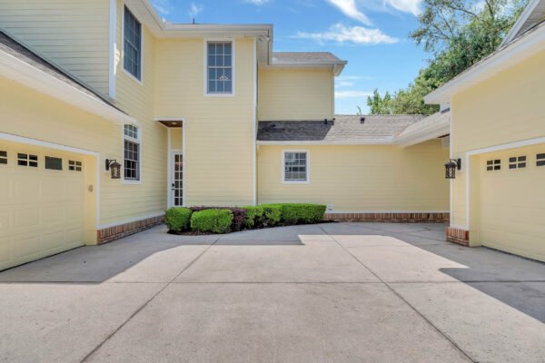 Yellow exterior of a custom-built estate at 6264 Blakeford Drive, Windermere, FL, featuring a landscaped entrance, driveway, and garage, emphasizing luxury living in a golf course community.