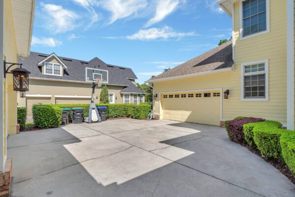 Driveway and garage area of a luxury home at 6264 Blakeford Drive, Windermere, FL, featuring neatly trimmed hedges and a spacious concrete surface, showcasing the property's well-maintained exterior and ample parking space.