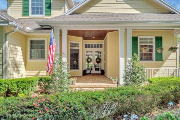 Front entrance of a custom-built estate at 6264 Blakeford Drive, Windermere, FL, featuring yellow exterior, green shutters, American flag, and landscaped garden.