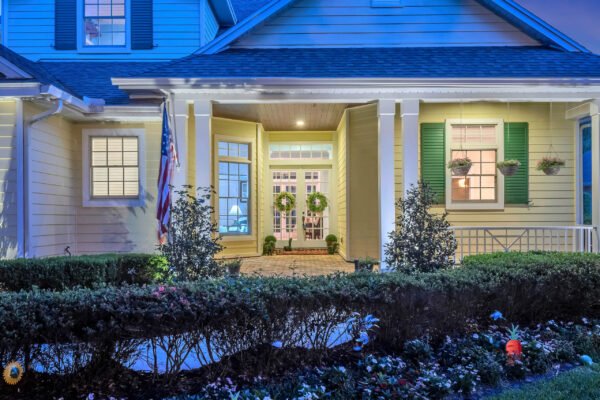 Front entrance of 6264 Blakeford Drive, Windermere, showcasing a welcoming porch, decorative wreaths on double doors, vibrant landscaping, and American flag, emphasizing the home's charm and curb appeal in a sought-after community.