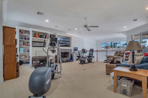 Spacious family room with exercise equipment, bookshelves, and cozy seating, showcasing a bright and inviting atmosphere in a custom-built estate at 6264 Blakeford Drive, Windermere, FL.