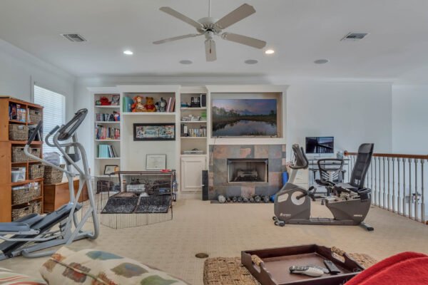Spacious home gym and entertainment area featuring exercise equipment, built-in bookshelves, a fireplace, and a view of the decorated living space, ideal for relaxation and fitness in the Windermere estate.