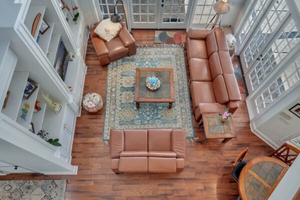 Spacious living room with leather sofas, coffee table, and decorative rug, featuring large windows and natural light, showcasing the elegant interior design of 6264 Blakeford Drive, Windermere, FL.