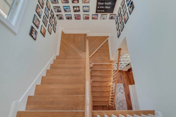 Staircase view with wooden steps and gallery wall of framed photos, showcasing a bright and inviting entryway in a custom-built home in Windermere, FL.