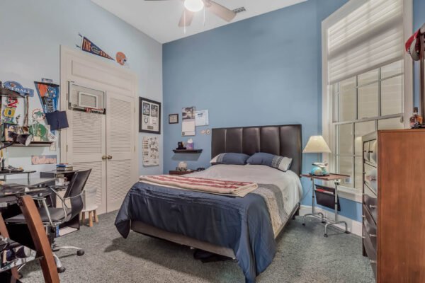 Cozy bedroom in Windermere, featuring a queen bed with blue bedding, a desk with a chair, and a window with natural light, ideal for a comfortable living space.
