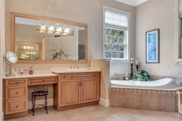 Luxurious bathroom with wooden cabinetry, double sink vanity, large mirror, soaking tub, and natural light from window, reflecting the elegance of the custom-built estate at 6264 Blakeford Drive in Windermere, FL.