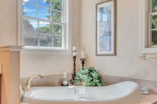 Elegant bathroom featuring a luxurious soaking tub, decorative plants, candle holders, and a large window with natural light illuminating the space, reflecting the upscale design of the Windermere estate at 6264 Blakeford Drive.