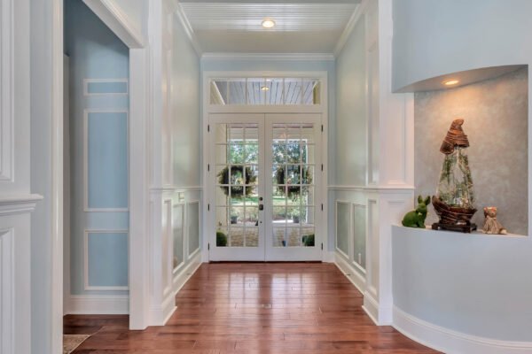 Elegant entryway of 6264 Blakeford Drive, Windermere, featuring hardwood floors, light blue walls, and double French doors opening to landscaped backyard views.