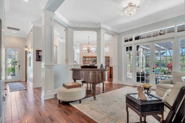 Elegant foyer with grand piano, hardwood floors, and natural light, leading to outdoor views and luxurious living space in custom estate at 6264 Blakeford Drive, Windermere, FL.
