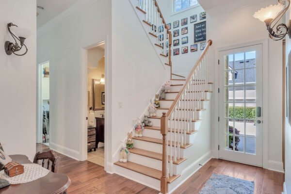 Elegant foyer of a custom-built estate at 6264 Blakeford Drive, featuring a staircase, decorative wall with family photos, and natural light from large windows, embodying a welcoming atmosphere in the Keenes Pointe community.