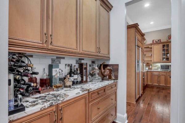 Elegant kitchen with custom cabinetry, granite countertops, wine rack displaying various bottles, and hardwood flooring, showcasing a luxurious design ideal for entertaining in the Windermere estate at 6264 Blakeford Drive.