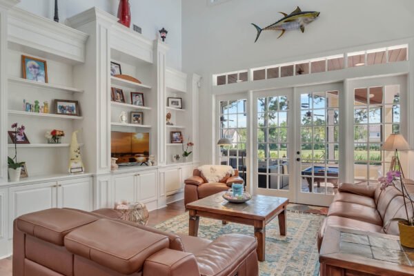 Living room interior of a custom-built estate in Windermere, featuring leather sofas, a wooden coffee table, built-in shelves with decor, and large windows offering views of the landscaped backyard and golf course.