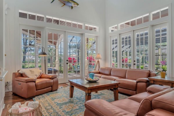 Spacious living room with leather sofas, wooden coffee table, and large windows showcasing lush outdoor views, highlighting the elegant design of the custom-built estate at 6264 Blakeford Drive, Windermere, FL.
