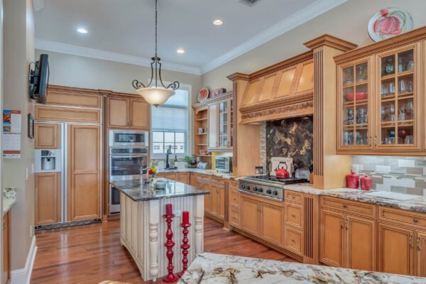 Custom kitchen with wooden cabinetry, granite countertops, and modern appliances, featuring an island with red candle holders, designed for entertaining in a luxury home.