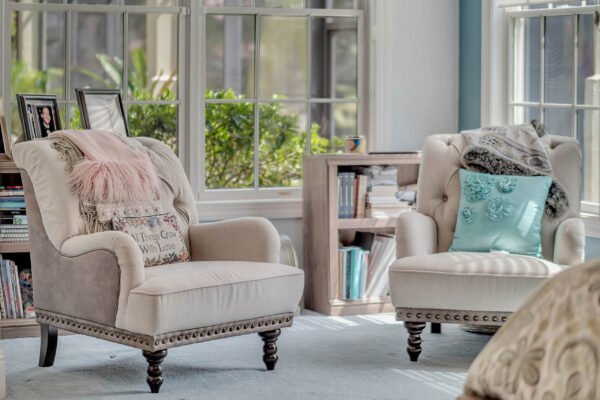 Cozy seating area with two elegant armchairs, one adorned with a decorative pillow and a throw blanket, surrounded by large windows and bookshelves, reflecting a bright and inviting atmosphere in a luxury Windermere home.