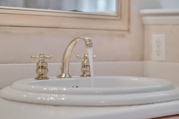 Elegant bathroom sink with polished gold faucet and running water, highlighting luxurious fixtures in a custom-built estate home.