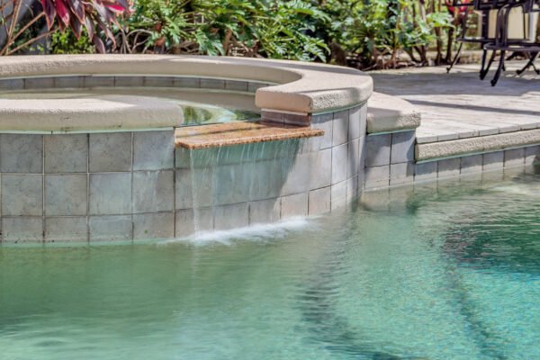 Spa area with waterfall feature in luxurious backyard pool setting, surrounded by lush landscaping, highlighting the outdoor entertainment potential of the property at 6264 Blakeford Drive, Windermere, FL.