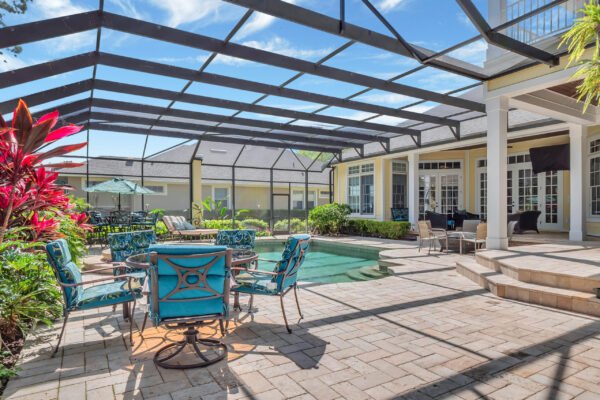Backyard oasis with pool and spa, surrounded by lush landscaping, featuring turquoise outdoor furniture and a screened enclosure, ideal for entertaining in Windermere, FL.