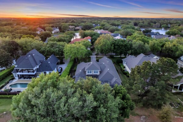 Aerial view of residential neighborhood in Windermere, Florida, showcasing luxury homes with lush landscaping and pools, under a sunset sky.
