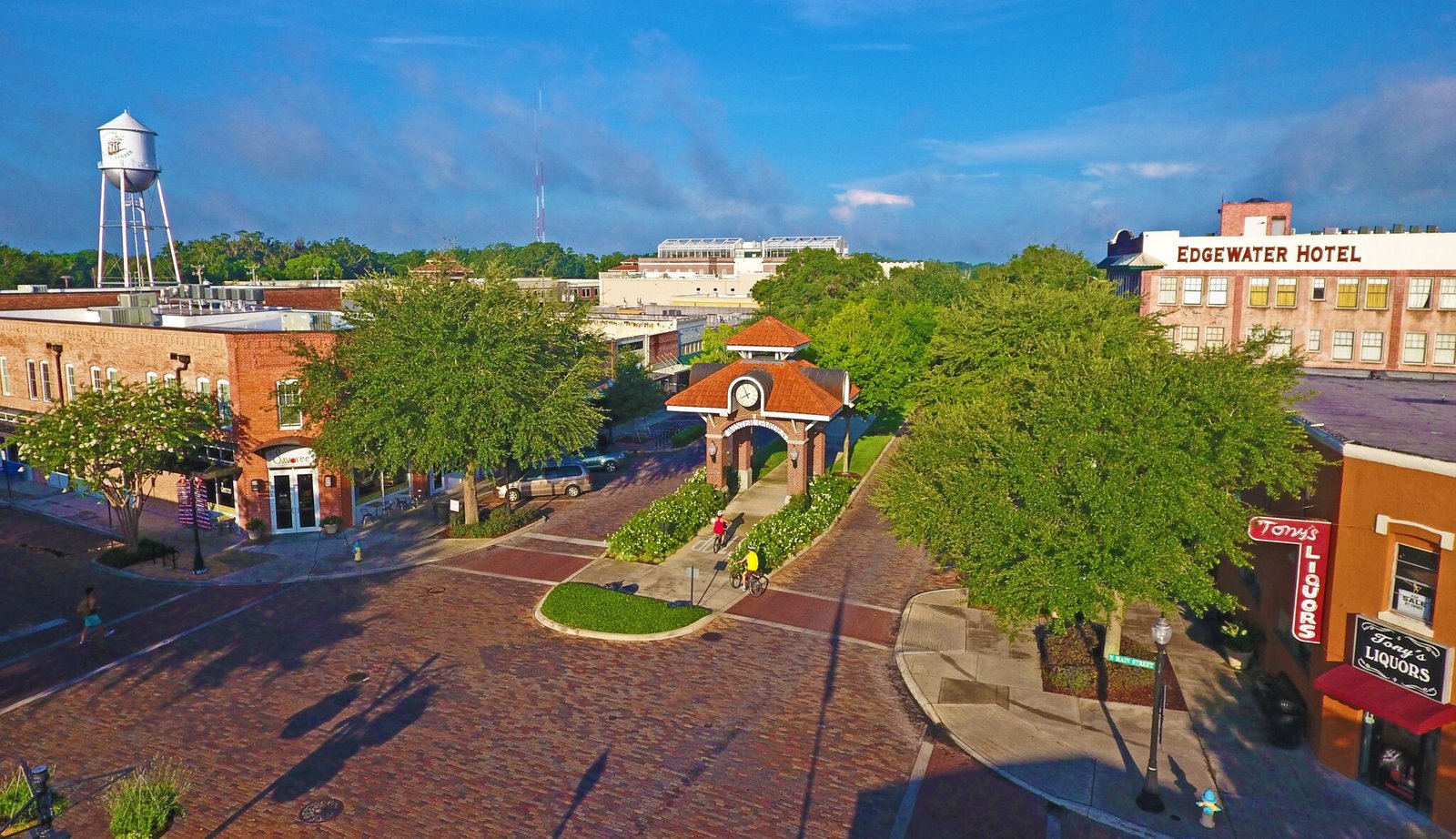 Aerial view of Winter Garden, Florida, featuring the Edgewater Hotel, historic buildings, a clock tower, and people biking on brick-paved streets surrounded by greenery.