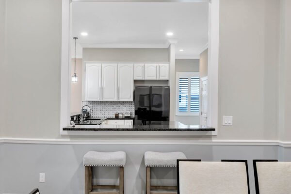 Modern kitchen view featuring white cabinetry, black appliances, and granite countertops, with a pass-through window and bar seating, showcasing the remodeled interior of a Windermere home.