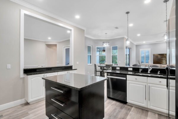 Modern gourmet kitchen featuring black granite countertops, white cabinetry, stainless steel appliances, and open layout with natural light from large windows, ideal for a remodeled home in Windermere, FL.