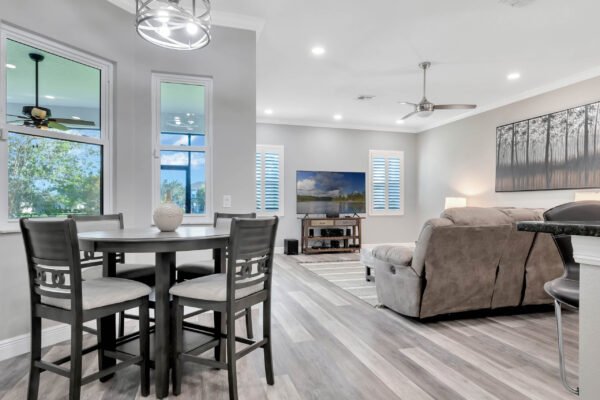 Modern living room and dining area in a remodeled Windermere home, featuring a circular dining table, plush sofa, large windows with natural light, and a wall-mounted TV, showcasing contemporary design and comfort.