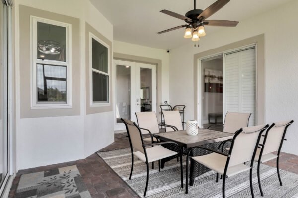 Covered patio with a table and chairs, modern ceiling fan, and large windows, showcasing outdoor living space at 13230 Fossick Road, Windermere, FL.