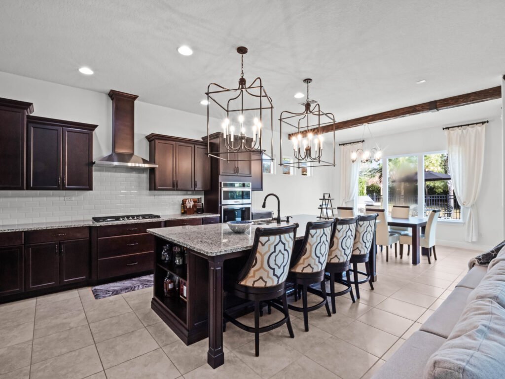 Modern kitchen featuring dark wood cabinetry, granite countertops, and stainless steel appliances, with a dining area visible through large windows, emphasizing the spacious layout ideal for Windermere real estate market insights.