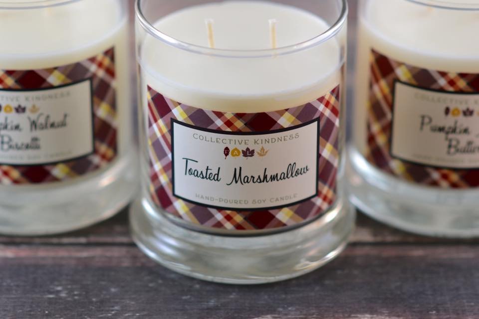 Toasted Marshmallow soy candle from Collective Kindness, featuring plaid label design, alongside other candle varieties, on wooden surface.