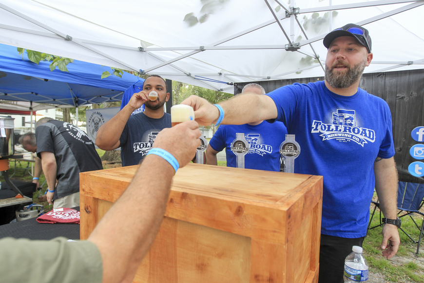 Toll Road Brewing Company staff serving craft beer at a festival, featuring a wooden bar and attendees enjoying drinks, emphasizing local brewing culture in Ocoee, Florida.
